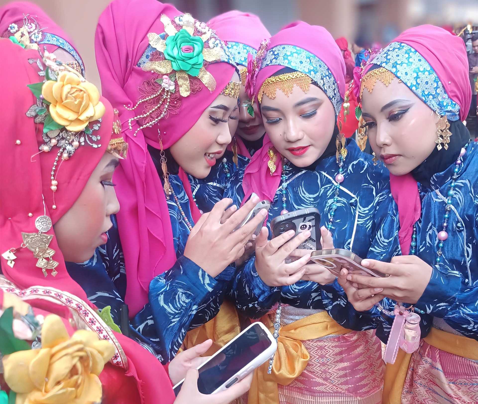 four young girls in bright pink Indonesian clothing looking at their phones