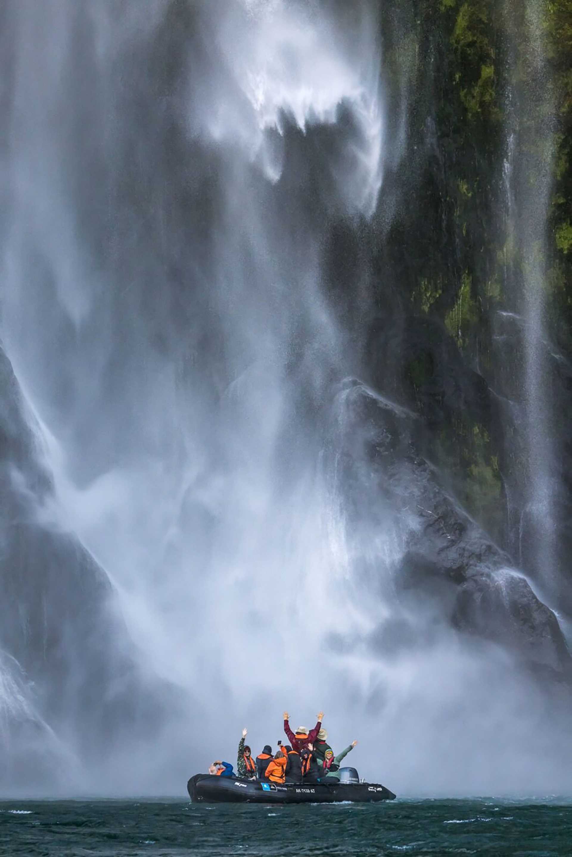 people in a zodiac under a waterfall