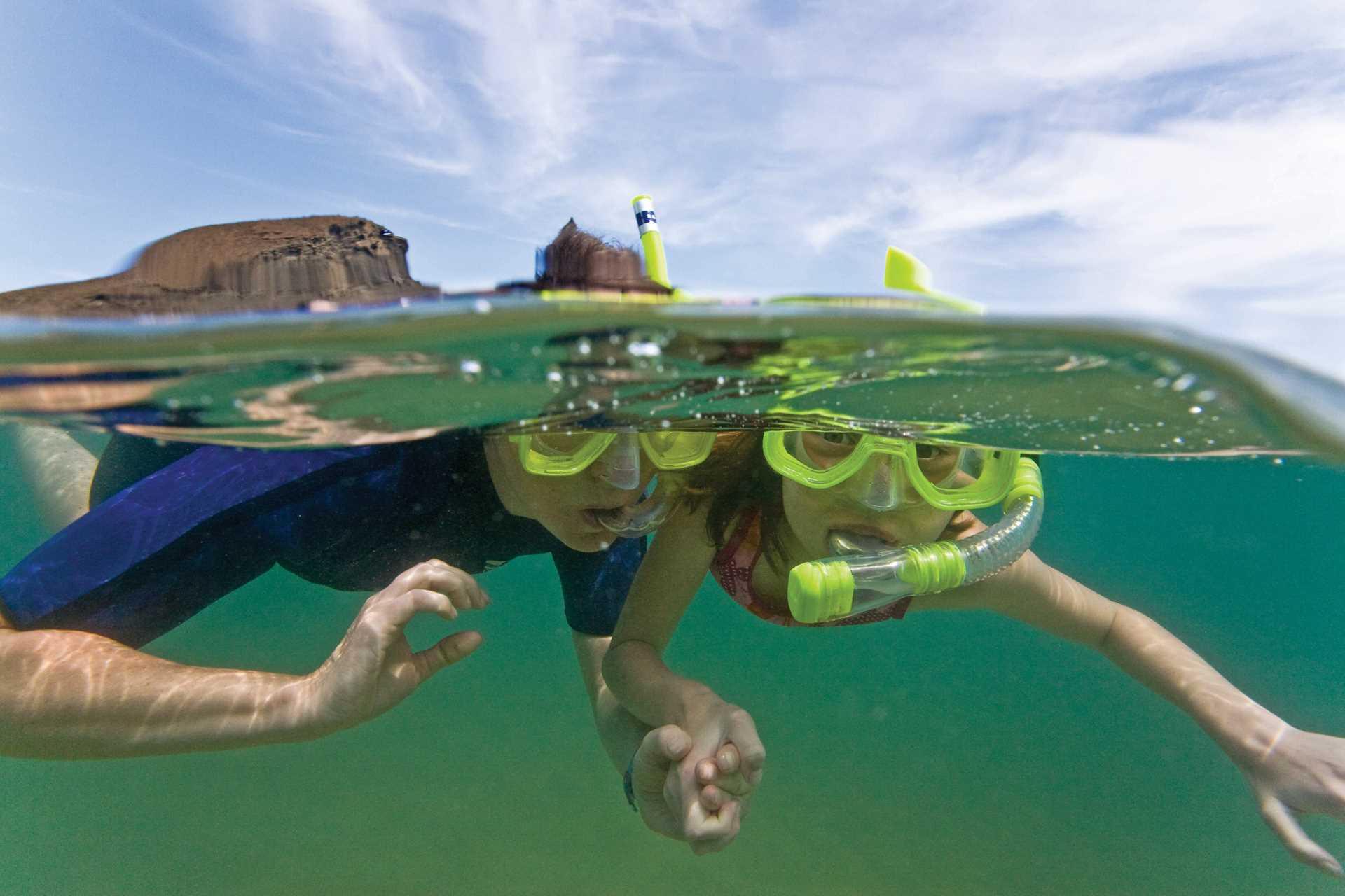 Two children hold hands while snorkeling.