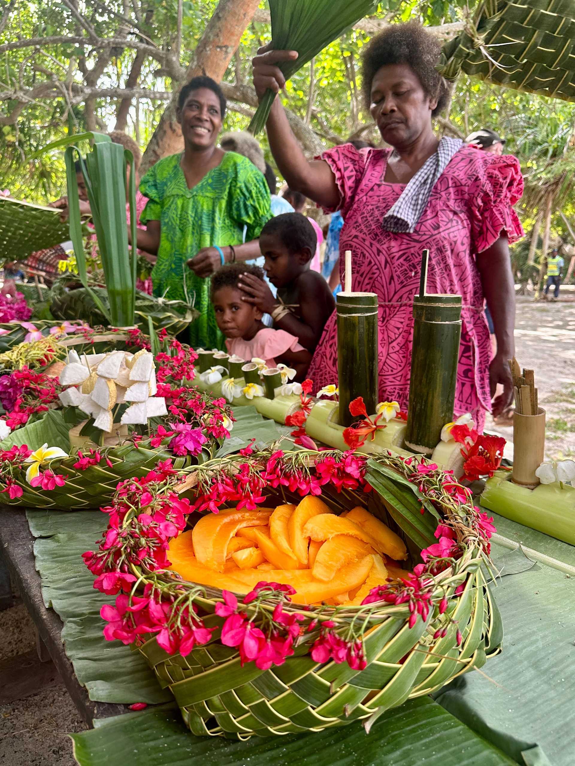 a woman in a bright pink dress serves orange fruit in a woven basket