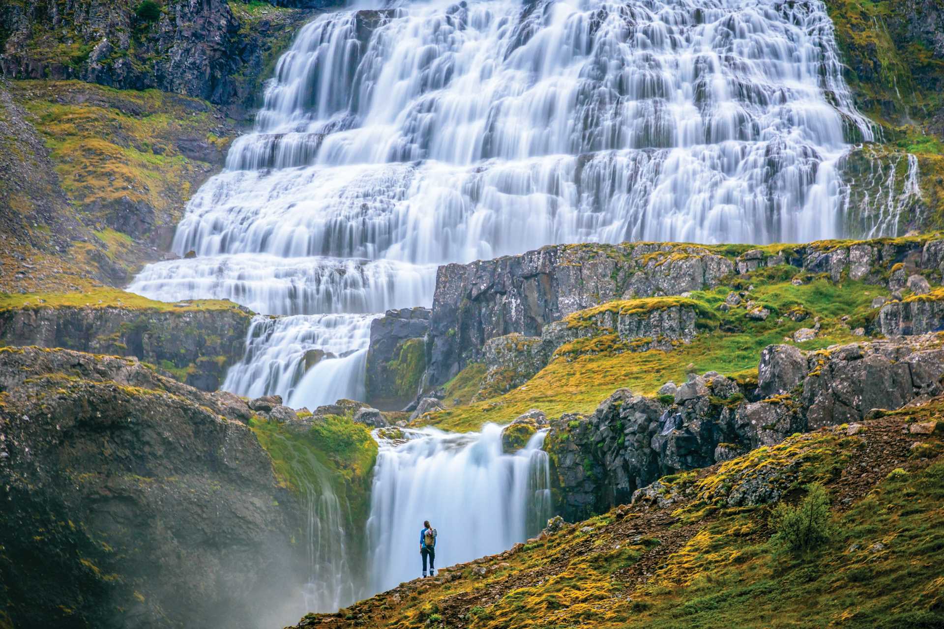 A hiker stands in front of the Dynjandi waterfall